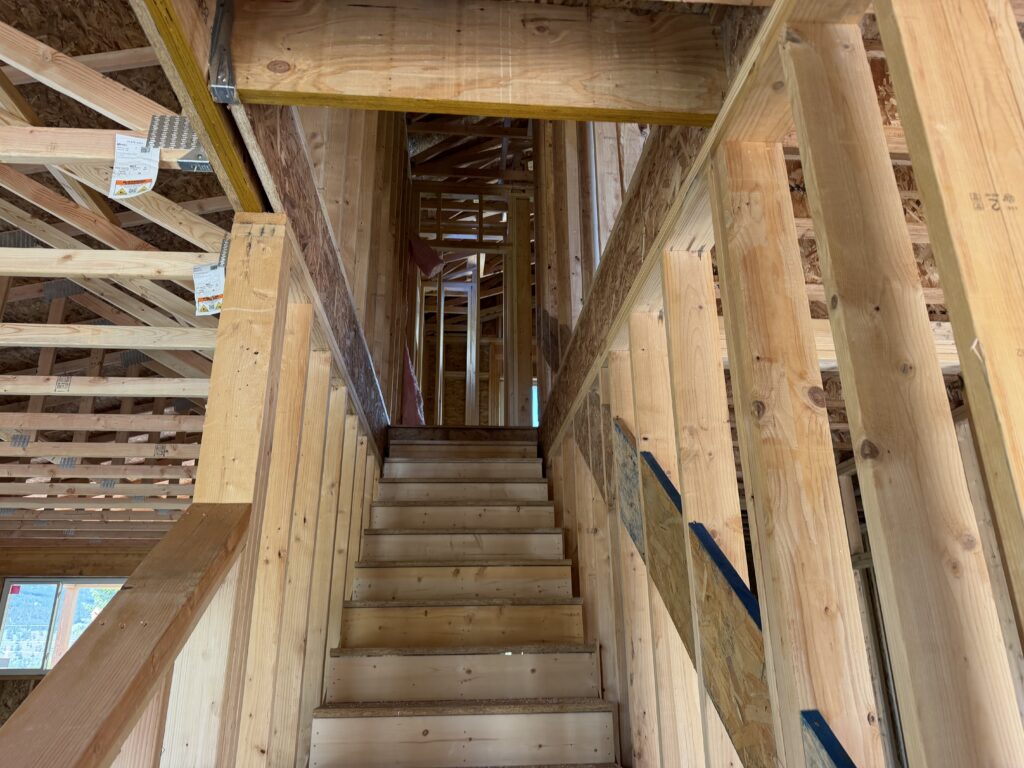 Interior of a townhouse under construction showing a wooden staircase, exposed framing, roof trusses, and OSB sheathing